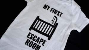 A photo showing a baby onesie with the phrase My First Escape Room.