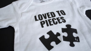 A photo showing a baby onesie with the phrase Loved To Pieces with puzzle pieces.